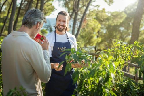 a man wearing an apron talking to a man in a garden at Porto Sani in Sani Beach