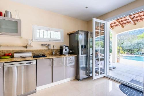 d'une cuisine équipée d'appareils en acier inoxydable et d'une porte coulissante en verre. dans l'établissement Villa Les Restanques - Piscine et Pétanque, à Rougiers