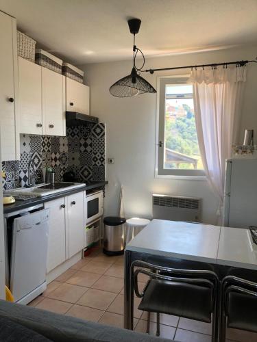 une cuisine avec des armoires blanches, une table et une fenêtre dans l'établissement Calme,mer, nature, à Bormes-les-Mimosas