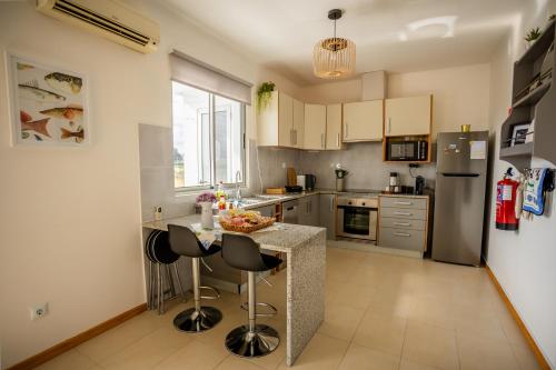 a kitchen with a counter with chairs and a refrigerator at Sentidos do Mar - Apartamento em São Miguel in Calhetas