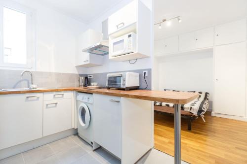 une cuisine avec des armoires blanches et une table avec un micro-ondes dans l'établissement Studio Maine - Montparnasse Paris 14th, à Paris