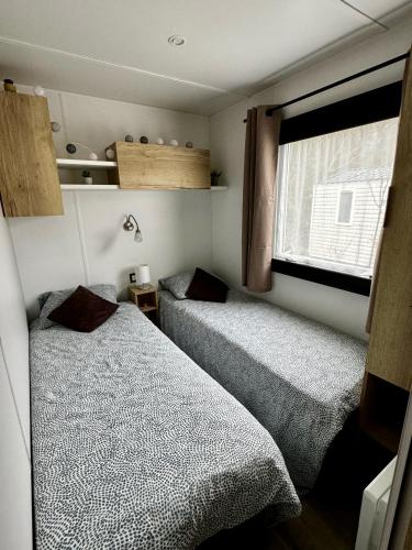 two beds in a small room with a window at Mobile-home 3 chambres chaleureux et calme in Seillac