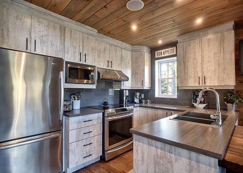 a kitchen with stainless steel appliances and wooden cabinets at Formidable Waterfront Cottage - Formidable Chalet sur bord de l'eau in Saint Come