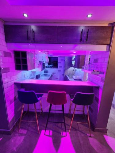 a kitchen with pink lighting and a bar with three stools at Durban Holiday Apartments , 1901 on High Tide in Amanzimtoti