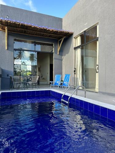 a swimming pool with blue chairs and a house at Casa Areia Bela - Patacho in Pôrto de Pedras