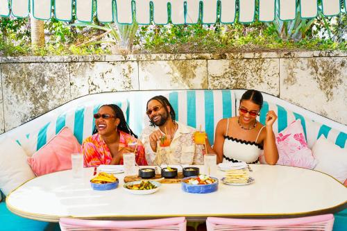 a group of three people sitting at a table with food at The Goodtime Hotel, Miami Beach a Tribute Portfolio Hotel in Miami Beach