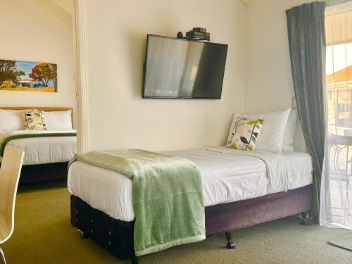 a room with two beds and a tv on the wall at The Olive Motel in Coromandel Town