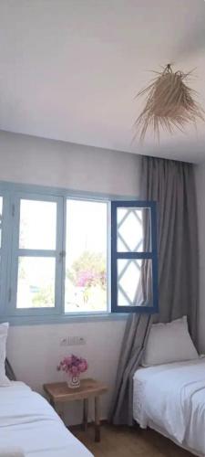 a bedroom with two beds and two windows at Appartement Les Vagues Uniquement les familles in Oualidia