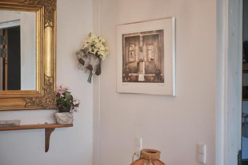 a wall with two pictures and a mirror and flowers at Askegaarden Apartments in Sandved