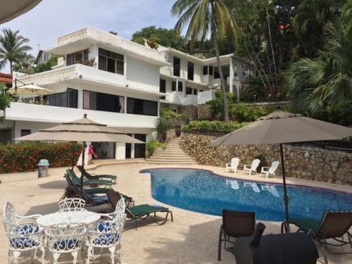 a pool with chairs and umbrellas in front of a building at Villa Panoramica 2 pisos, piscina vista al mar in Acapulco