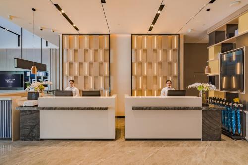 two women sitting at reception desks in a lobby at Echarm International Hotel Guangzhou South Railway Station Zhongcun Metro Station Branch - Free Shuttle Bus to Canton Fair Complex During Canton Fair Period & Free Deliver Service to Guangzhou Baiyun International Airport in Guangzhou