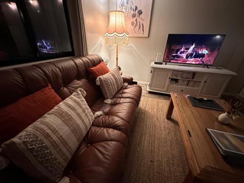 a living room with a brown leather couch and a television at The Hide, Bouvard in Dawesville