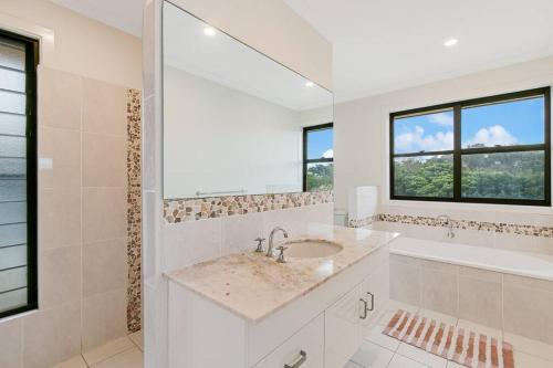 a white bathroom with a sink and a tub andwindows at Serenity at Salt - Beachside Beauty by uHoliday in Kingscliff