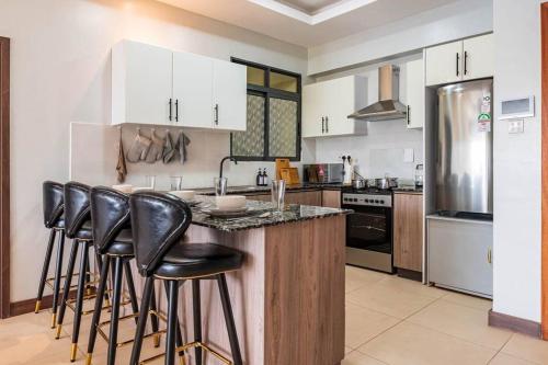 a kitchen with a bar with stools at a counter at Lush Retreat Near Yaya Center with Pool, Gym & Views in Nairobi