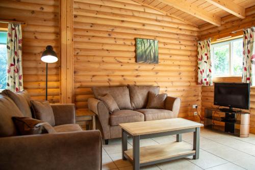 Cabaña con sala de estar con sofá y TV. en Quail Lodge - Nordic Log Cabin, en Selby