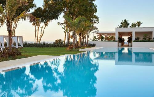 a swimming pool in front of a house with palm trees at Ikos Andalusia in Estepona