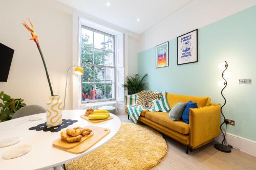 a living room with a table and a yellow couch at Stay Kula London - Covent Garden Opera House in London