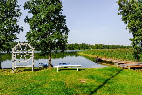 a white bench sitting on the grass next to a lake at Namelis ant ežero kranto "Giliaus Elingas" in Tytuvėnai
