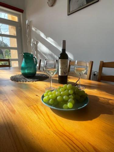 a plate of grapes on a wooden table with a bottle of wine at Csomópont Családi Vendégház in Somogytúr