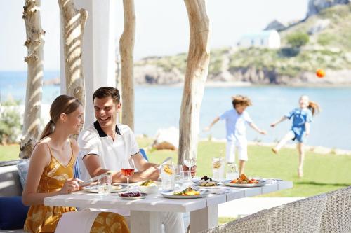 a man and a woman sitting at a table with food at Ikos Aria in Kefalos