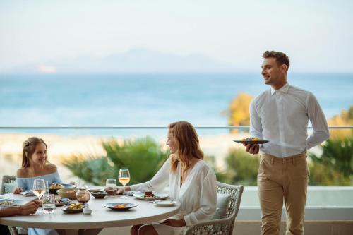 a group of people sitting around a table with a man holding a plate at Ikos Aria in Kefalos