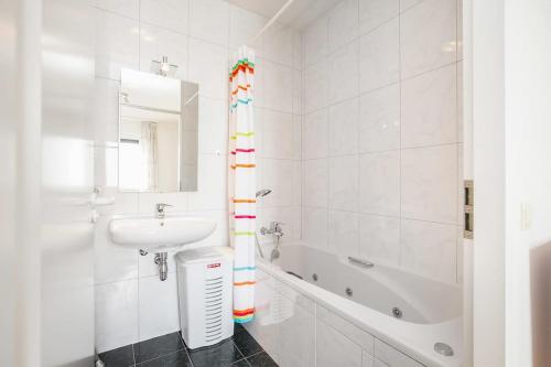 a white bathroom with a sink and a bath tub at Hello Zeeland - Appartement Port Scaldis 13-112 in Breskens