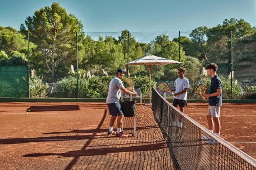 four men standing on a tennis court holding rackets at Ikos Aria in Kefalos