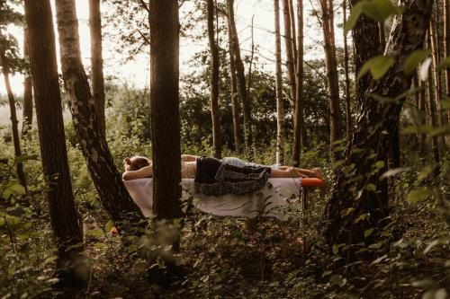 a person laying on a bed in the woods at Jurty z widokiem, prywatna balia- DZIKOLAS GLAMPING in Krasnobród