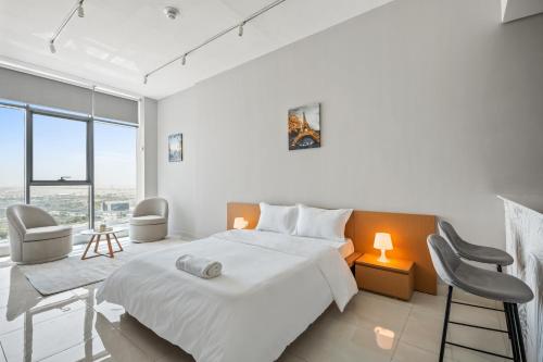 a white bedroom with a large bed and chairs at Bright Studio In Vibrant Dubailand District in Dubai