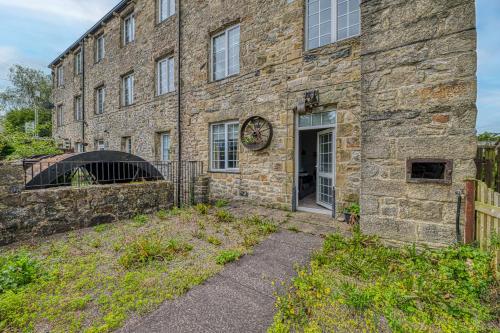 an old stone building with a door and a fence at Bridge End Mill by Guestz in Settle