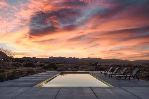 a pool with chairs and a sunset in the background at The Raven By The Cohost Company in Pioneertown