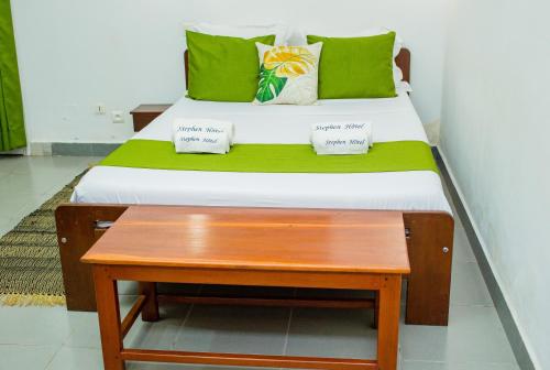 a bed with green pillows and a wooden table at STEPHEN HOTEL in Toamasina
