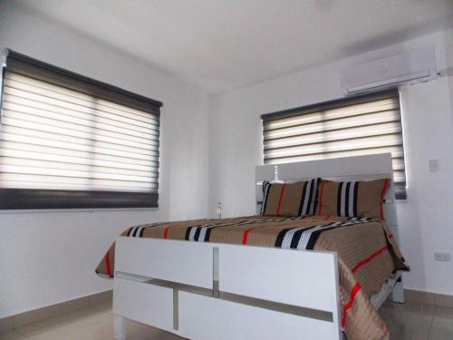 a white bedroom with a bed and two windows at Cañaveral Del Mar 1 Quiet and extremally relaxing! in San Felipe de Puerto Plata