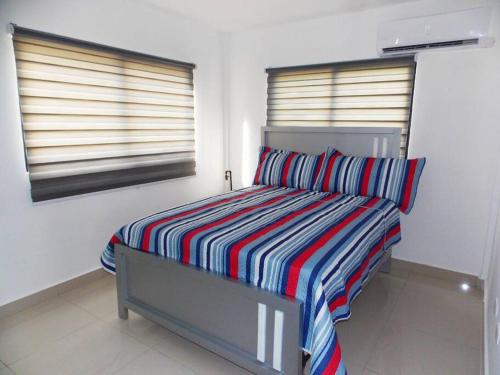 a bedroom with a bed with a striped blanket and two windows at Cañaveral Del Mar 1 Quiet and extremally relaxing! in San Felipe de Puerto Plata