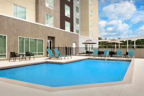 a swimming pool with blue chairs and a building at TownePlace Suites Jacksonville Airport in Jacksonville