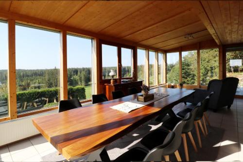 une grande table en bois et des chaises dans une pièce avec des fenêtres dans l'établissement Fewo "Alpenliebe" im Haus Fritz, 3 Schlafzimmer, E-Auto-Ladestation, Eisenbach, Titisee, à Oberbränd