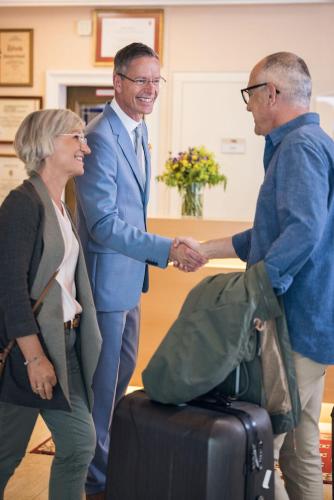 two men and a woman shaking hands next to a suitcase at Hotel Sportalmmm, Hoch-Genuss in Zauchensee