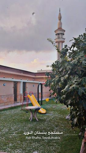a playground with a building with a clock tower at شاليهات بستان الورد لبيوت العطلات in Al Shafa