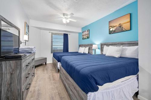 a blue bedroom with two beds and a television at Luxury 17th Floor 1 BR Condo Direct Oceanfront Wyndham Ocean Walk Resort Daytona Beach | 1708 in Daytona Beach