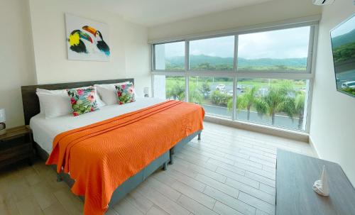 a bedroom with a bed with an orange blanket and a large window at Sanctuary by Playa Caracol Residences in Punta Chame