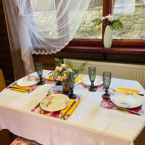 a white table with plates and glasses and flowers on it at Еко котедж Яблуницька троянда in Yablunytsya