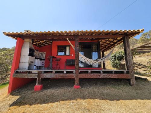 a red house with a hammock in front of it at Chalés Vila Real - Tranquilidade na Serra de Carrancas - Piscina com uma vista espetacular do Pôr do Sol in Carrancas