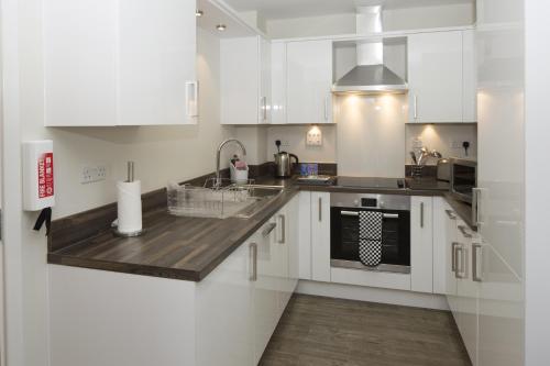 a kitchen with white cabinets and a sink and a stove at House of Fisher - Beneficial House in Bracknell