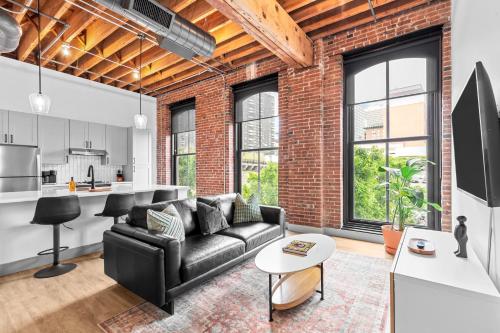 a living room with a black couch and a brick wall at Brick & Bed Riverfront Lofts, G 201 in Saint Louis