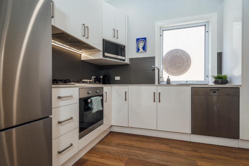 a kitchen with white cabinets and a window at Belle Escapes - Moseley Apartments near the beach with private garden in Glenelg