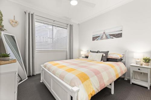 a white bedroom with a bed and a window at The Bayswood Retreat on Moona Creek by Experience Jervis Bay in Vincentia