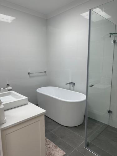 a white bathroom with a tub and a glass shower at Surfleet Retreat Kiama in Kiama