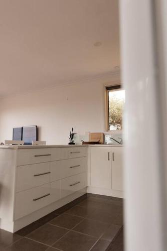 a kitchen with white cabinets and a window at Tides & Tails - Pet Friendly in Scamander