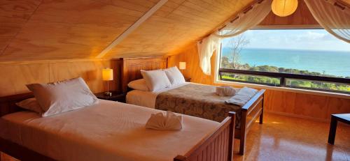 a bedroom with two beds and a large window at Tawa Whare holiday accommodation in Raglan