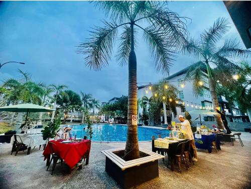 a restaurant with tables and a palm tree next to a pool at Royal Homestay Palm Garden in Lahad Datu